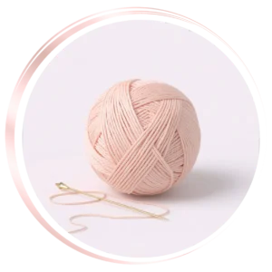 3D yarn ball with golden needle inside soft pink circular frame representing handmade creations